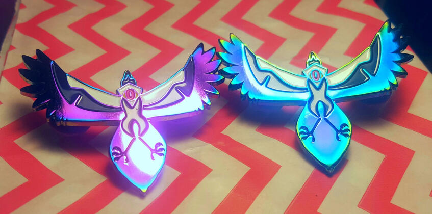 Magp-eye Pins, rainbow plated soft enamel pins depicting a magpie with an eye in its neck.