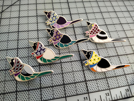 Birdbushka Set 1, a set of hard enamel pins depicting songbirds wearing babushka-style head scarves.
